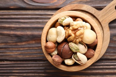 Photo of Mix of different nuts in bowl on wooden table, top view. Space for text