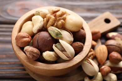 Photo of Mix of different nuts in bowl on wooden table, closeup