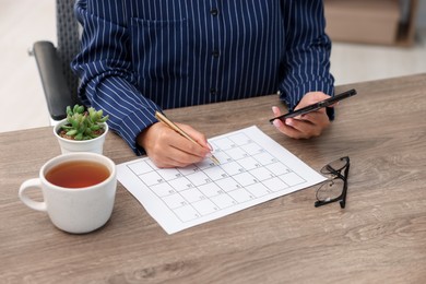 Photo of Woman using business planner and smartphone at wooden desk, closeup