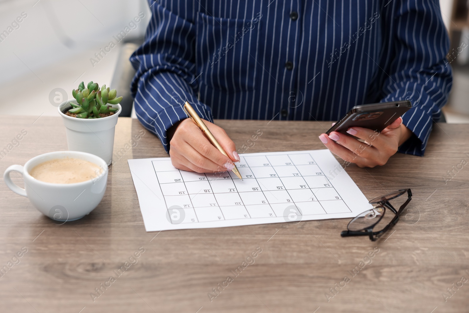 Photo of Woman using business planner and smartphone at wooden desk, closeup