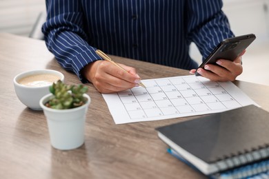 Photo of Woman using business planner and smartphone at wooden desk, closeup