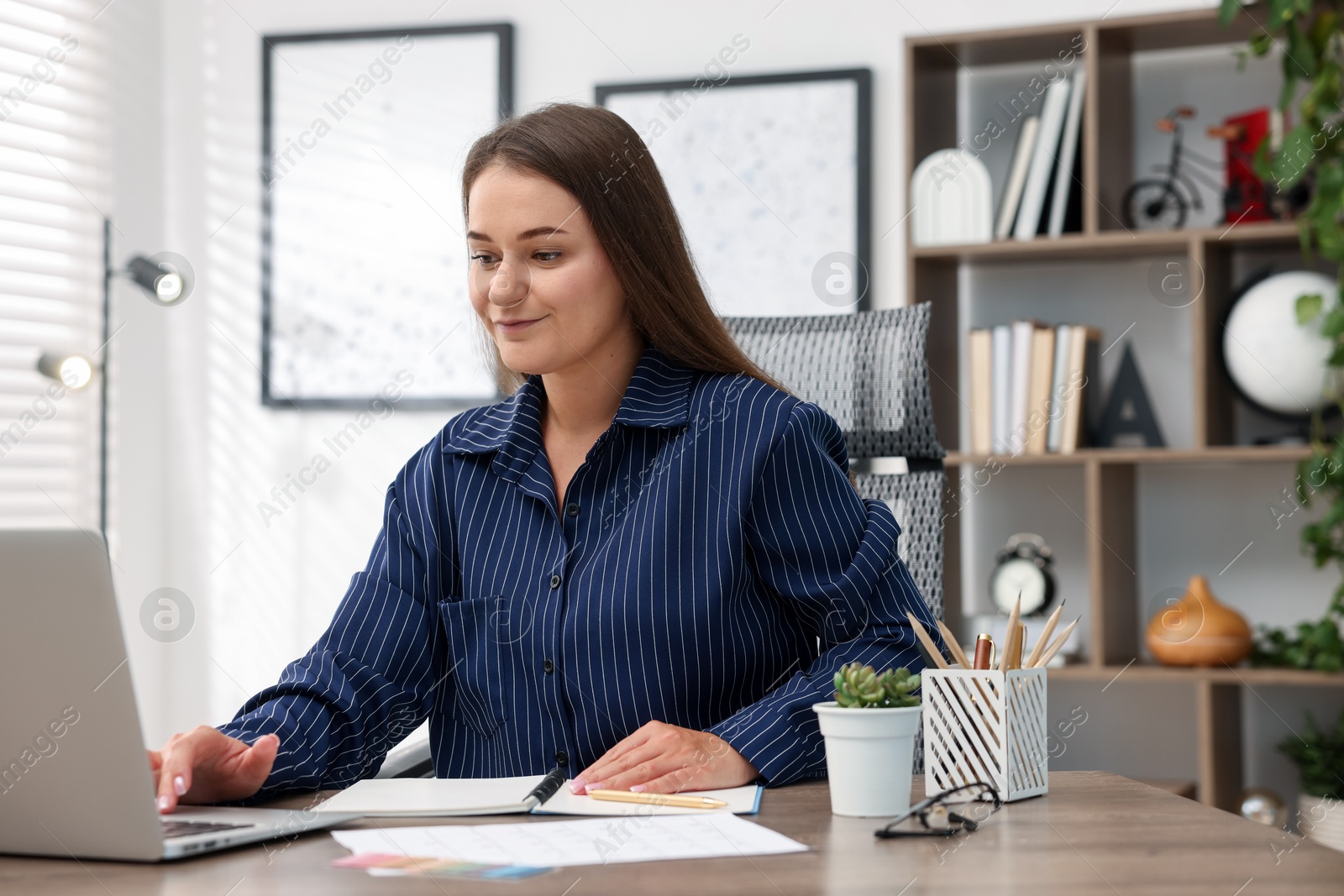 Photo of Woman with planner using laptop at desk in office