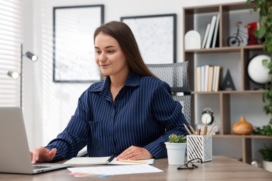 Photo of Woman with planner using laptop at desk in office