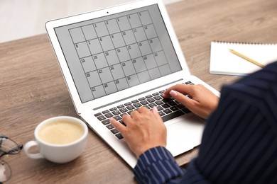 Photo of Woman using business planner on laptop at wooden desk, closeup