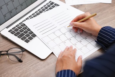 Photo of Woman writing in business planner at wooden desk, closeup