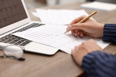 Photo of Woman writing in business planner at wooden desk, closeup