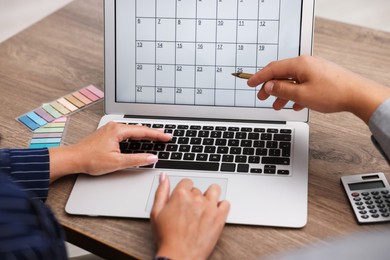 Photo of Woman and man using business planner on laptop at wooden desk, closeup