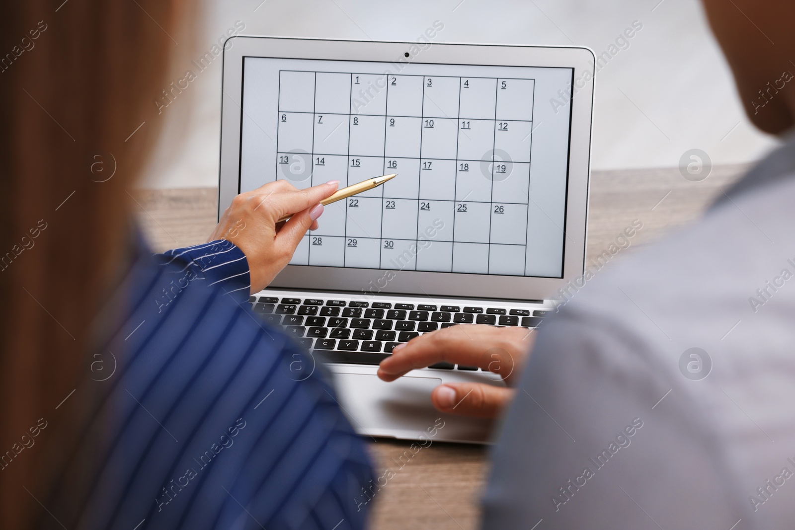 Photo of Woman and man using business planner on laptop at wooden desk, closeup