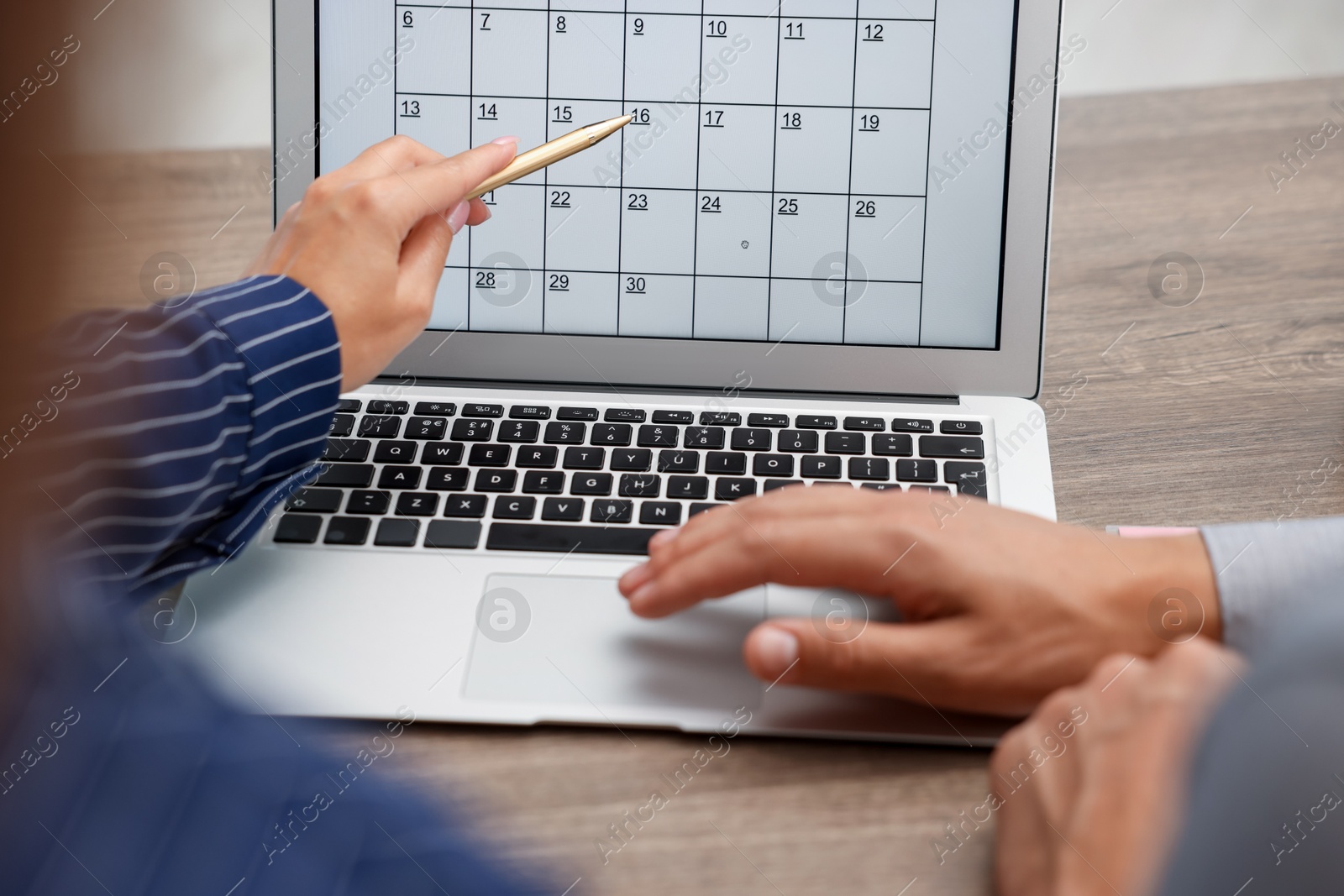 Photo of Woman and man using business planner on laptop at wooden desk, closeup