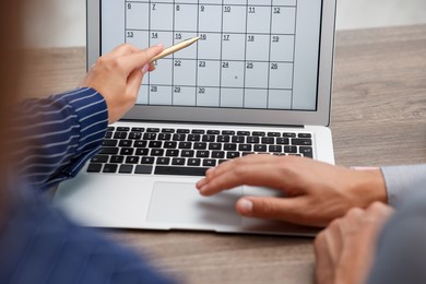 Photo of Woman and man using business planner on laptop at wooden desk, closeup