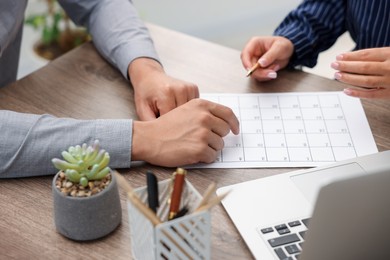 Photo of Woman and man using business planner at wooden desk, closeup