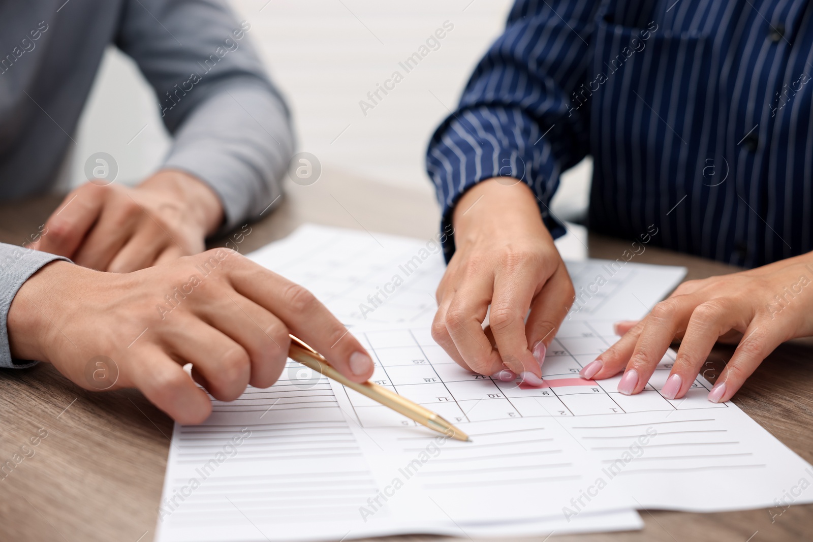 Photo of Woman and man using business planner at wooden desk, closeup