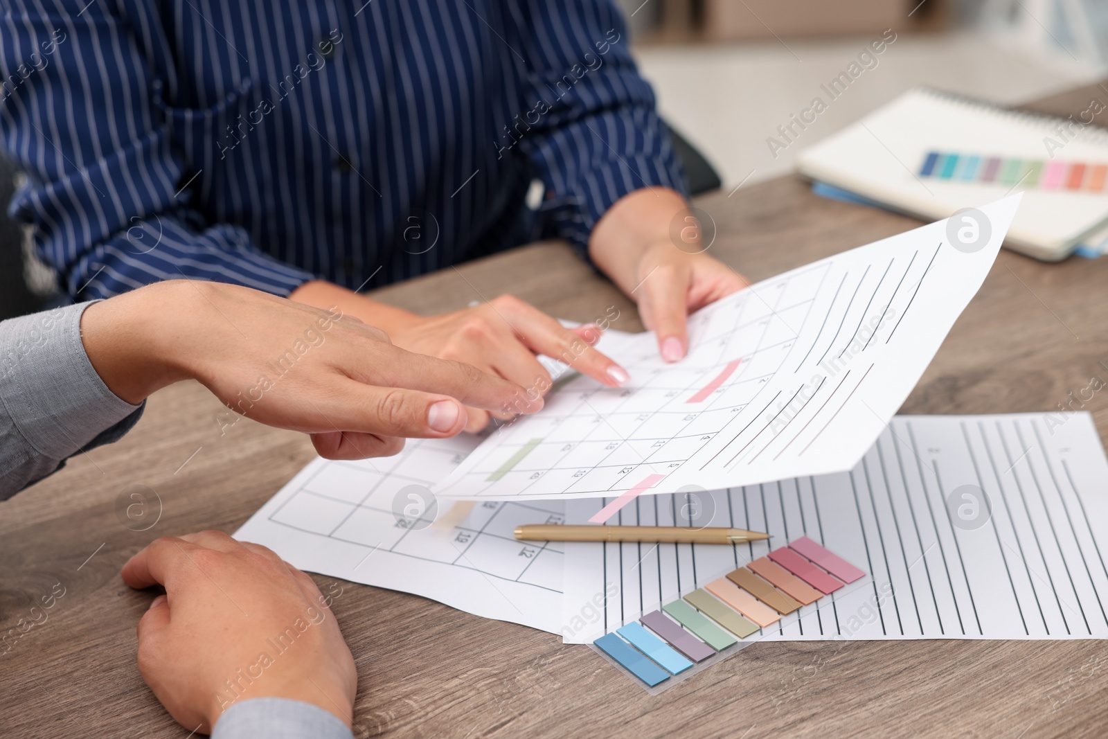 Photo of Woman and man using business planner at wooden desk, closeup