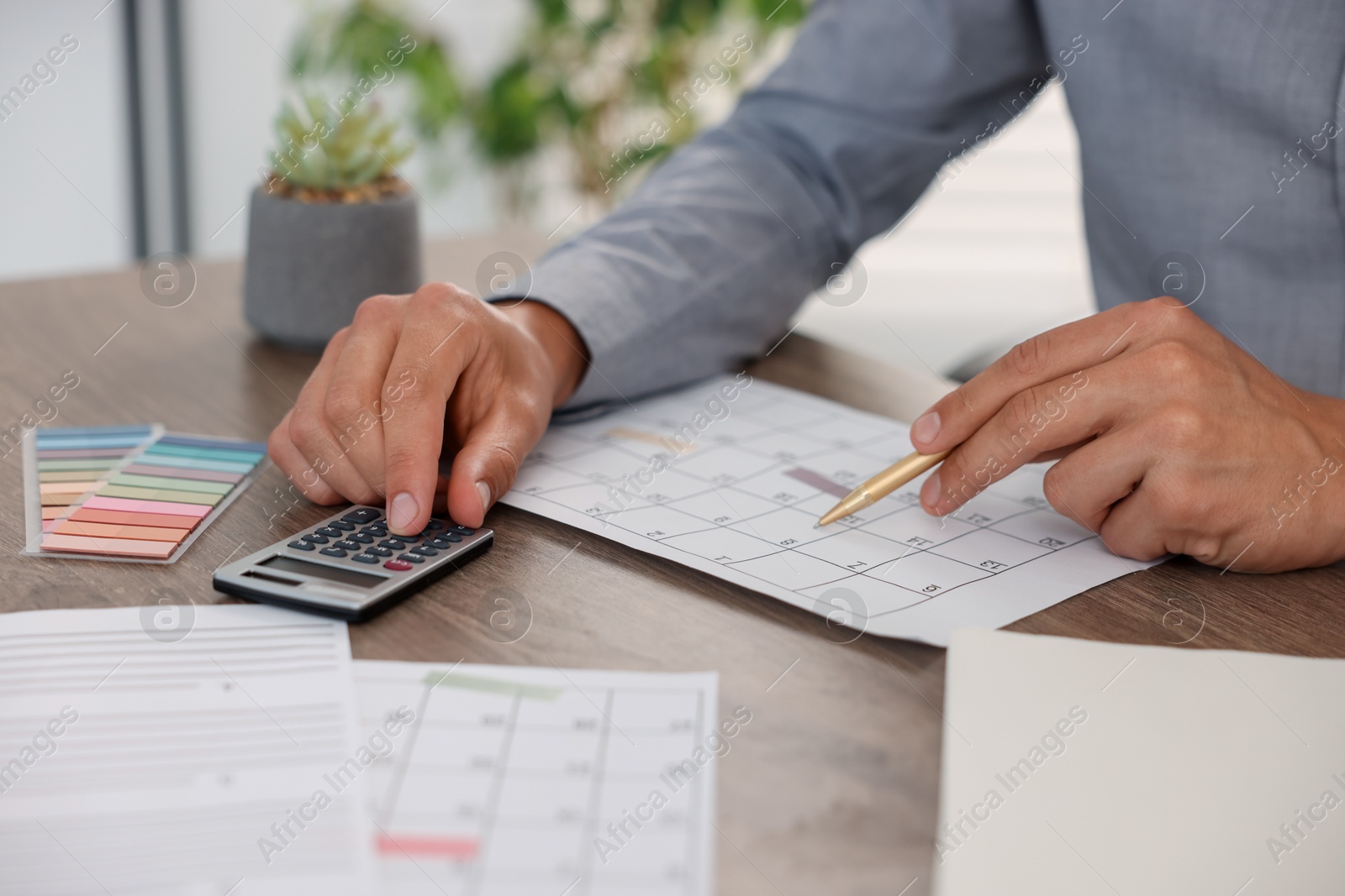 Photo of Man using business planner and calculator at wooden desk, closeup