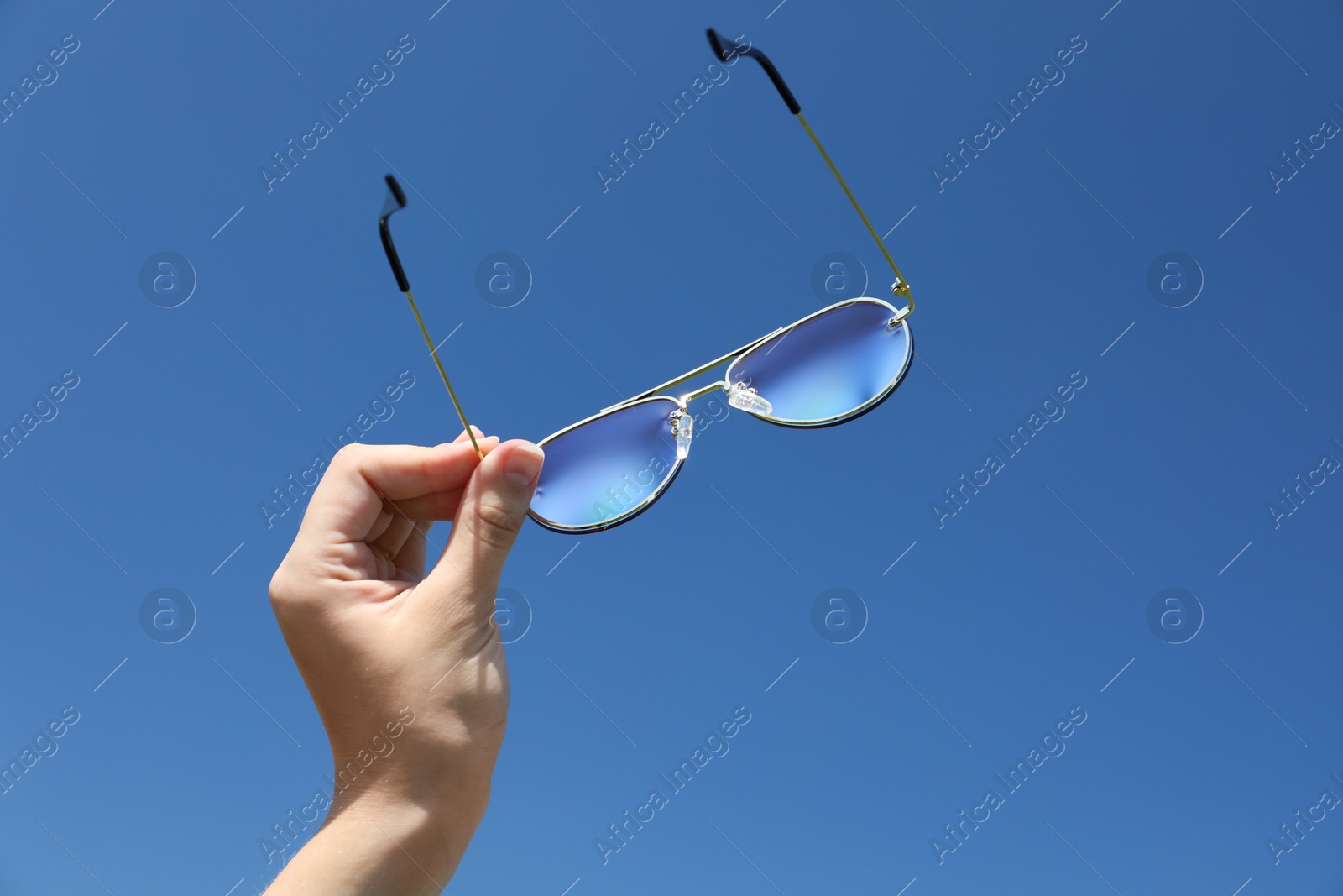 Photo of Woman holding stylish sunglasses against blue sky, low angle view