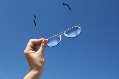 Photo of Woman holding stylish sunglasses against blue sky, low angle view