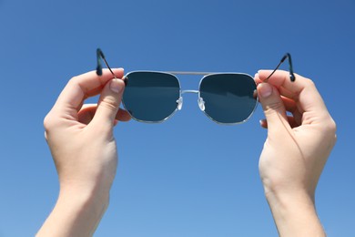 Photo of Woman holding stylish sunglasses against blue sky, closeup