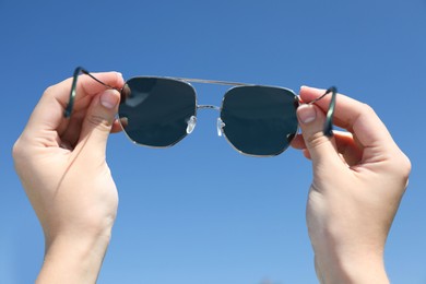 Photo of Woman holding stylish sunglasses against blue sky, closeup