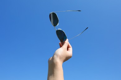 Photo of Woman holding stylish sunglasses against blue sky, closeup