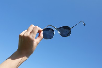 Photo of Woman holding stylish sunglasses against blue sky, closeup