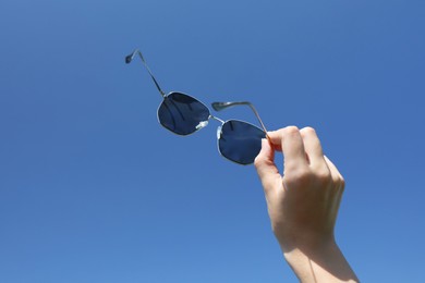 Photo of Woman holding stylish sunglasses against blue sky, closeup
