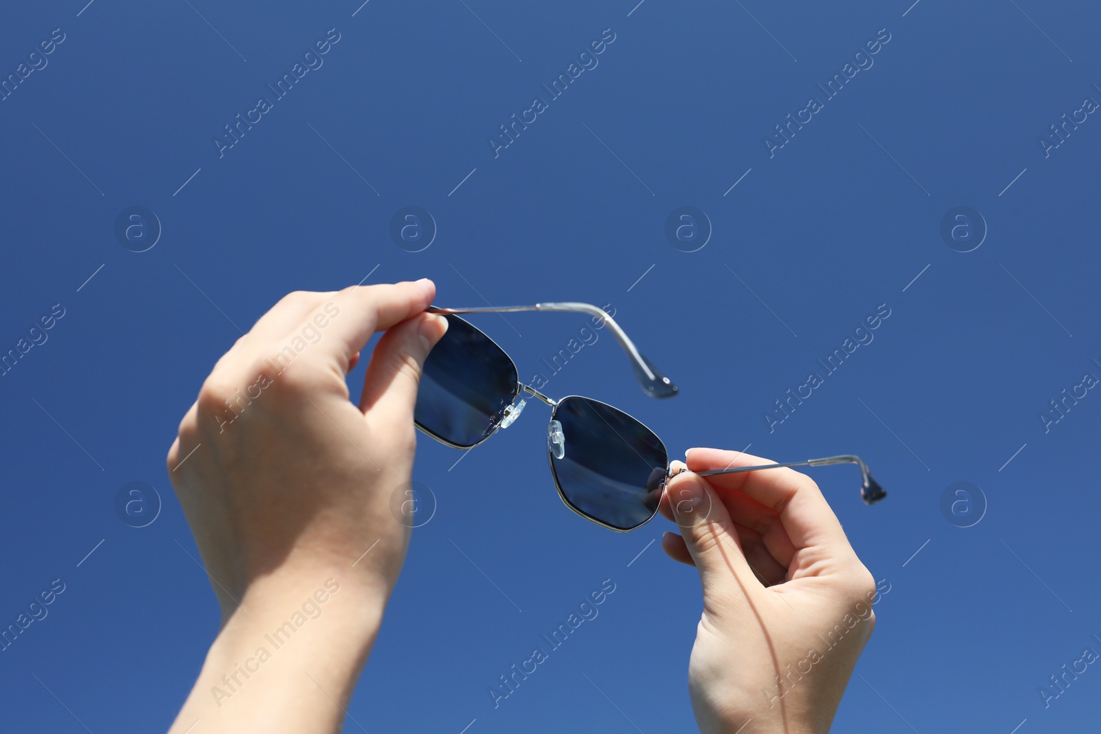 Photo of Woman holding stylish sunglasses against blue sky, low angle view