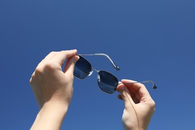 Photo of Woman holding stylish sunglasses against blue sky, low angle view