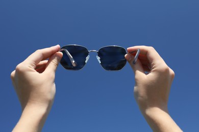 Photo of Woman holding stylish sunglasses against blue sky, low angle view