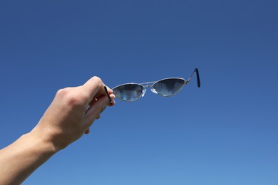 Photo of Woman holding stylish sunglasses against blue sky, closeup