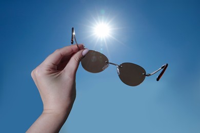 Photo of Woman holding stylish sunglasses against blue sky, closeup