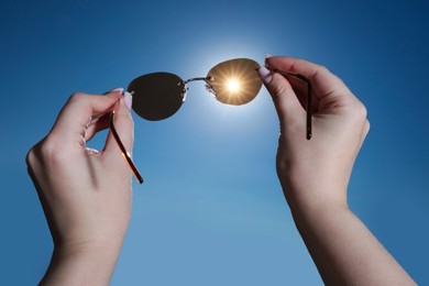 Photo of Woman holding stylish sunglasses against shiny sun, closeup
