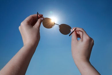 Photo of Woman holding stylish sunglasses against shiny sun, closeup