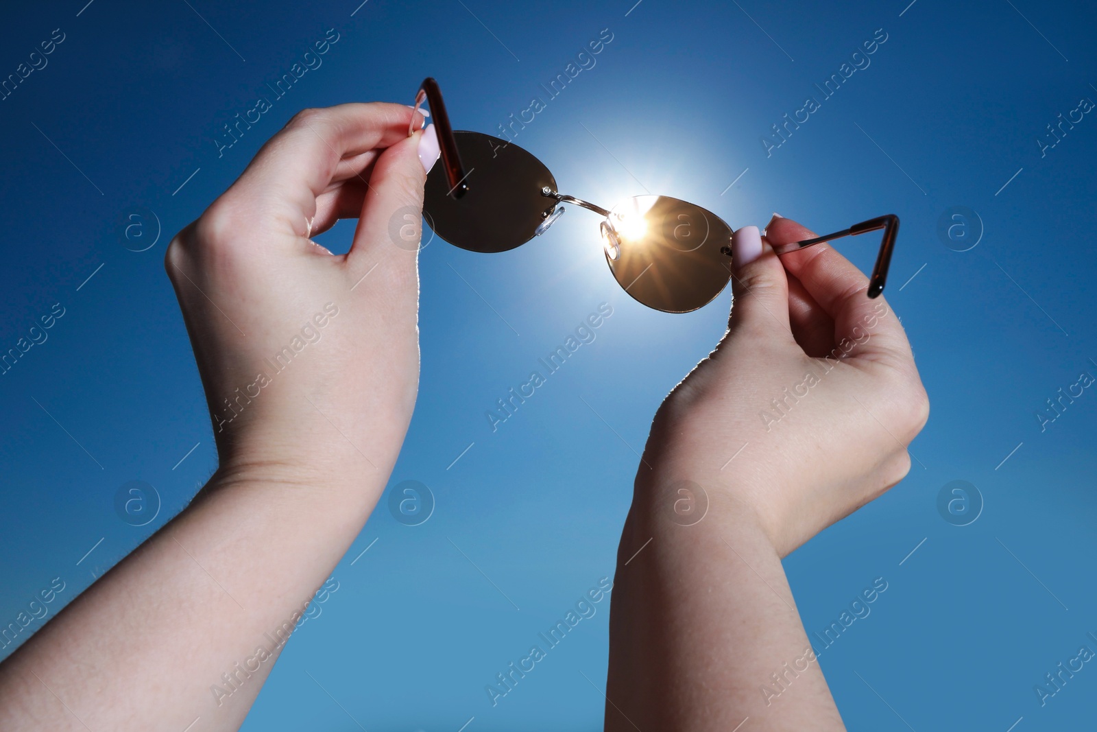Photo of Woman holding stylish sunglasses against shiny sun, closeup