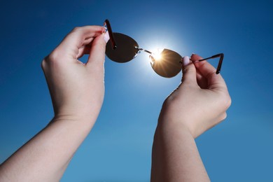 Photo of Woman holding stylish sunglasses against shiny sun, closeup