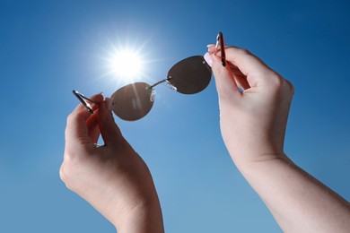 Photo of Woman holding stylish sunglasses against shiny sun, closeup