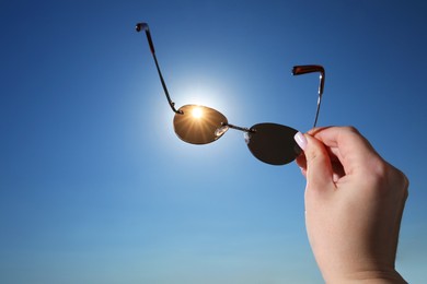 Photo of Woman holding stylish sunglasses against shiny sun, closeup. Space for text