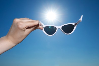 Photo of Woman holding stylish sunglasses against blue sky, closeup