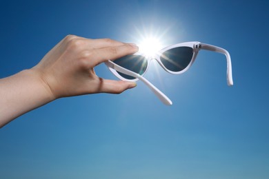 Photo of Woman holding stylish sunglasses against shiny sun, closeup