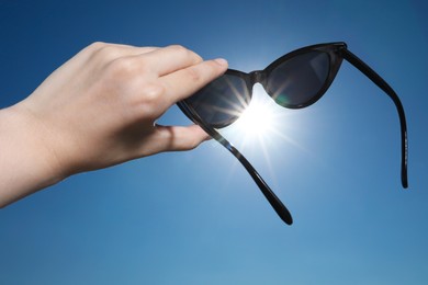 Photo of Woman holding stylish sunglasses against shiny sun, closeup
