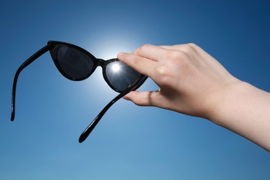 Photo of Woman holding stylish sunglasses against shiny sun, closeup