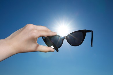 Photo of Woman holding stylish sunglasses against shiny sun, closeup