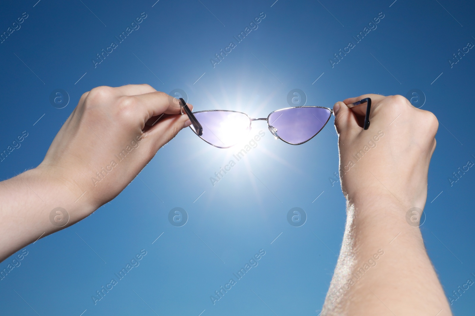 Photo of Woman holding stylish sunglasses against shiny sun, closeup