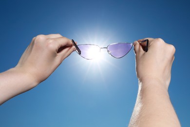 Photo of Woman holding stylish sunglasses against shiny sun, closeup