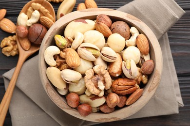 Photo of Mix of different nuts in bowl and spoon on wooden table, flat lay