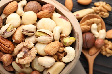 Photo of Mix of different nuts in bowl and spoon on wooden table, flat lay