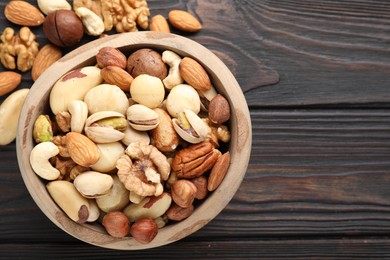 Photo of Mix of different nuts in bowl on wooden table, flat lay. Space for text