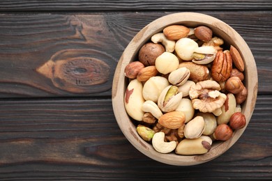 Photo of Mix of different nuts in bowl on wooden table, top view. Space for text