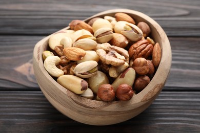 Photo of Mix of different nuts in bowl on wooden table, closeup