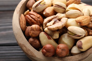 Photo of Mix of different nuts in bowl on wooden table, closeup