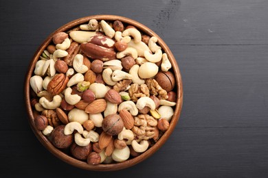 Photo of Mix of different nuts in bowl on black wooden table, top view. Space for text